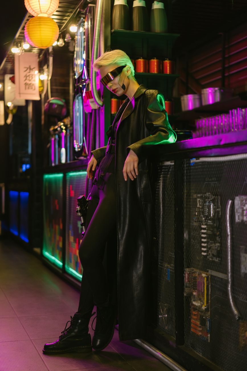 A woman in futuristic attire with visor eyewear stands in a neon-lit cyberpunk bar.
