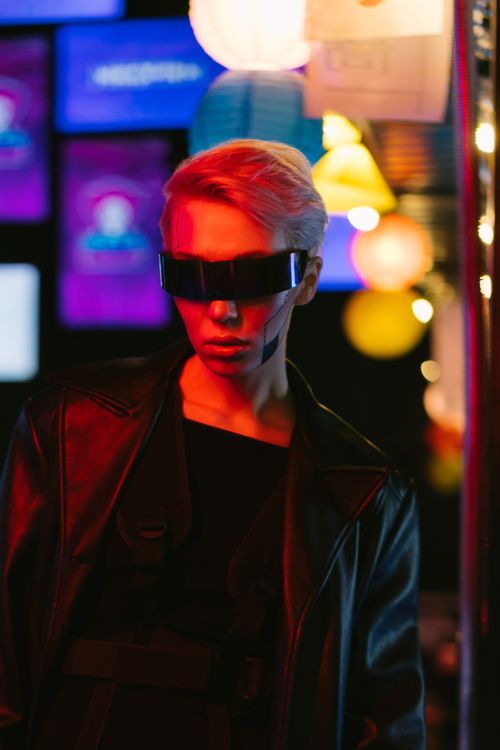 Free A stylish woman in cyberpunk attire and sunglasses against colorful neon lights. Stock Photo