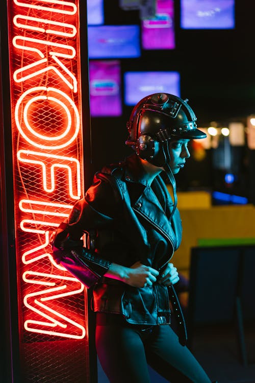 Woman in Black Leather Jacket Standing Beside a Neon Signage