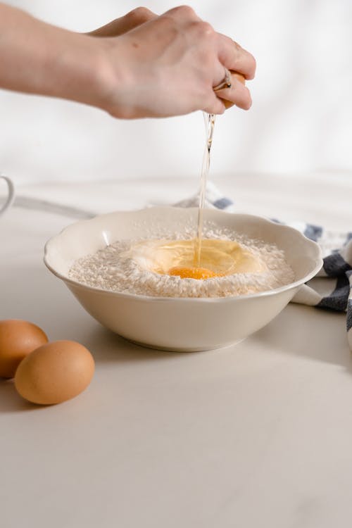 Free Person Cracking Egg and Putting it on Bowl of Flour Stock Photo