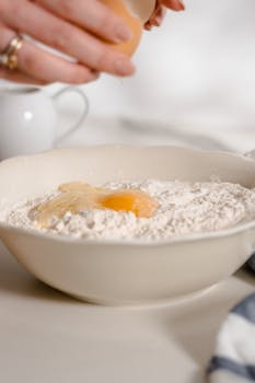 Preparing ingredients for homemade baking with raw egg and flour in a ceramic bowl.