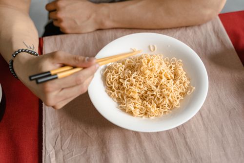 Free A person holding chopsticks ready to eat noodles from a white bowl at a table. Stock Photo