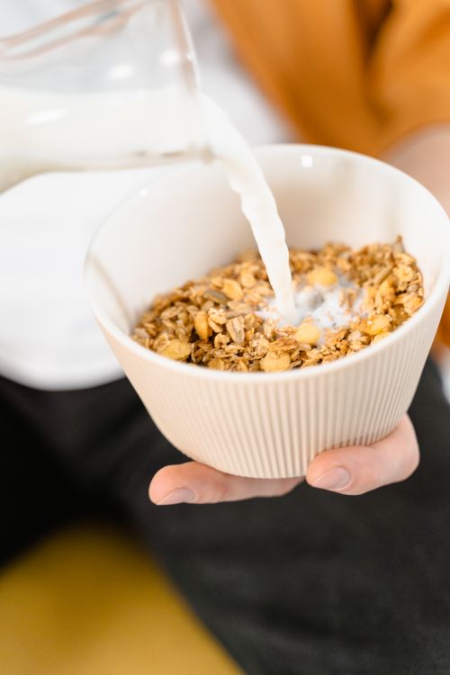 Free Delicious granola cereal with milk being poured into a white ceramic bowl in a close-up shot. Stock Photo