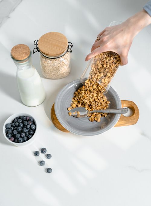 Free High-angle view of granola being poured into a bowl with milk and blueberries. Stock Photo