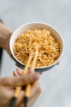 Close-up of a bowl of instant noodles being held with chopsticks, ideal for food concept.