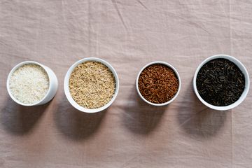 Four white bowls of white, brown, red and black wild rice in a row