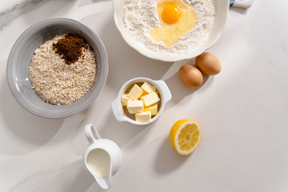 Prep bowls of spices, grain, butter, eggs and lemon laid out on a white marble counter — MART PRODUCTION on Pexels