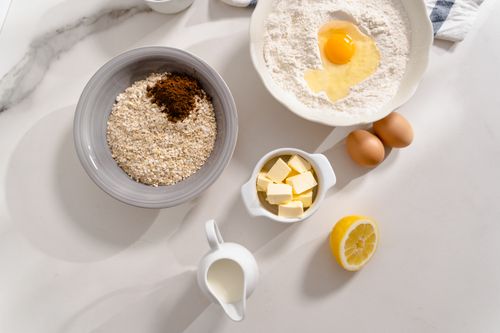 Free An overhead shot of baking ingredients including flour, eggs, butter, milk, and spices on a white counter. Stock Photo