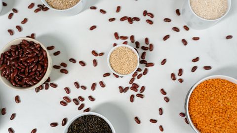 Top view of various grains and pulses in bowls on a white surface.