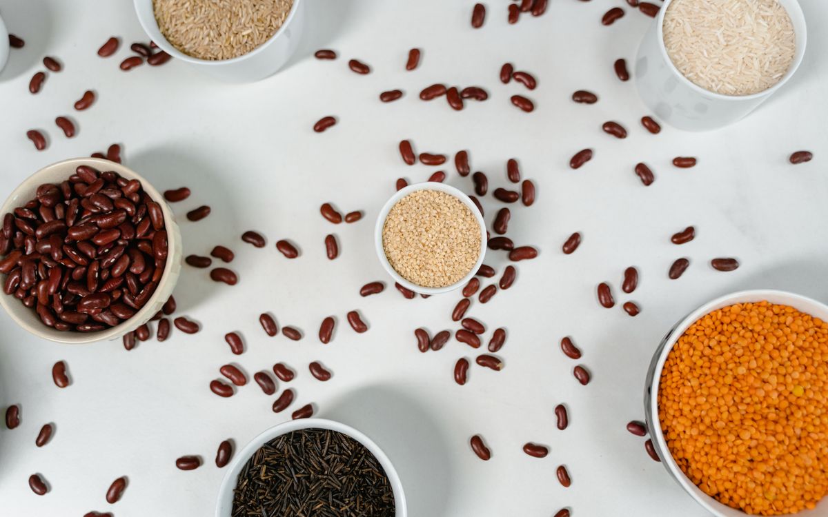 Top view of various grains and pulses in bowls on a white surface.