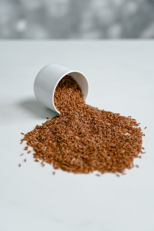 Free A close-up of organic brown rice spilling from a white cup on a solid background. Stock Photo