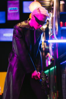 Person in cyberpunk attire with neon lights, wearing a leather coat and eyewear.