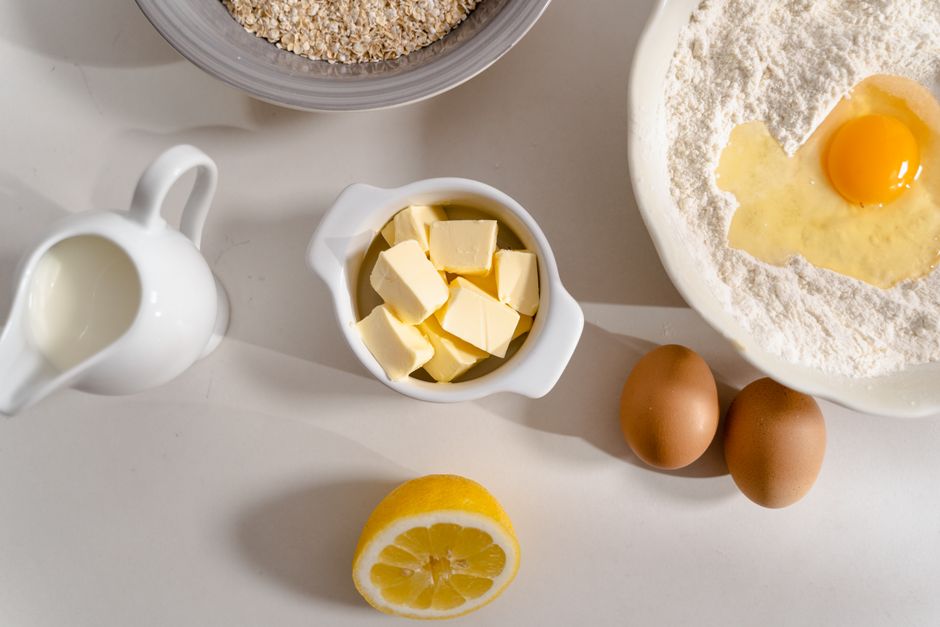 Sticks of butter and a carton of eggs sitting out on a wooden countertop next to a small kitchen thermometer