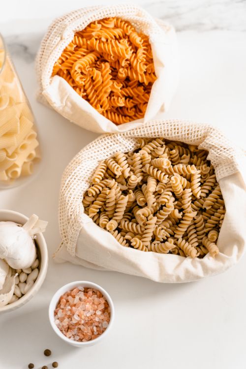 Free Eco-friendly flat lay of assorted pasta, garlic, and salt in reusable bags. Stock Photo
