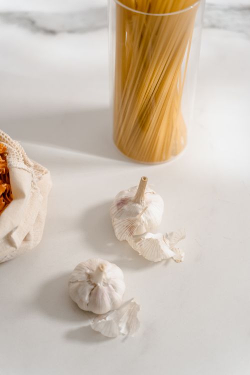 Free High-angle view of garlic bulbs, dry spaghetti, and pasta ingredients on a light kitchen counter. Stock Photo
