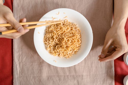 A Person Holding a Chopstick Near the Noodles on a Ceramic Bowl