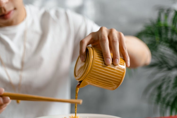 Person Pouring Liquid From A Ceramic Container