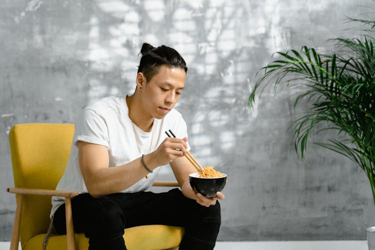 Man Sitting On Chair Eating With Noodles