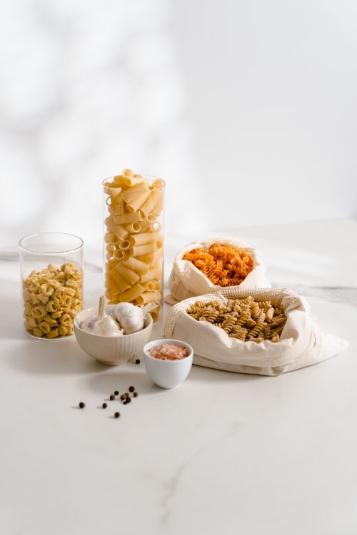 Free Assorted uncooked pasta with garlic, pink salt, and peppercorns on a white backdrop. Stock Photo