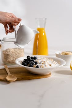 A delicious breakfast with oatmeal, blueberries, and milk being poured, accompanied by orange juice.