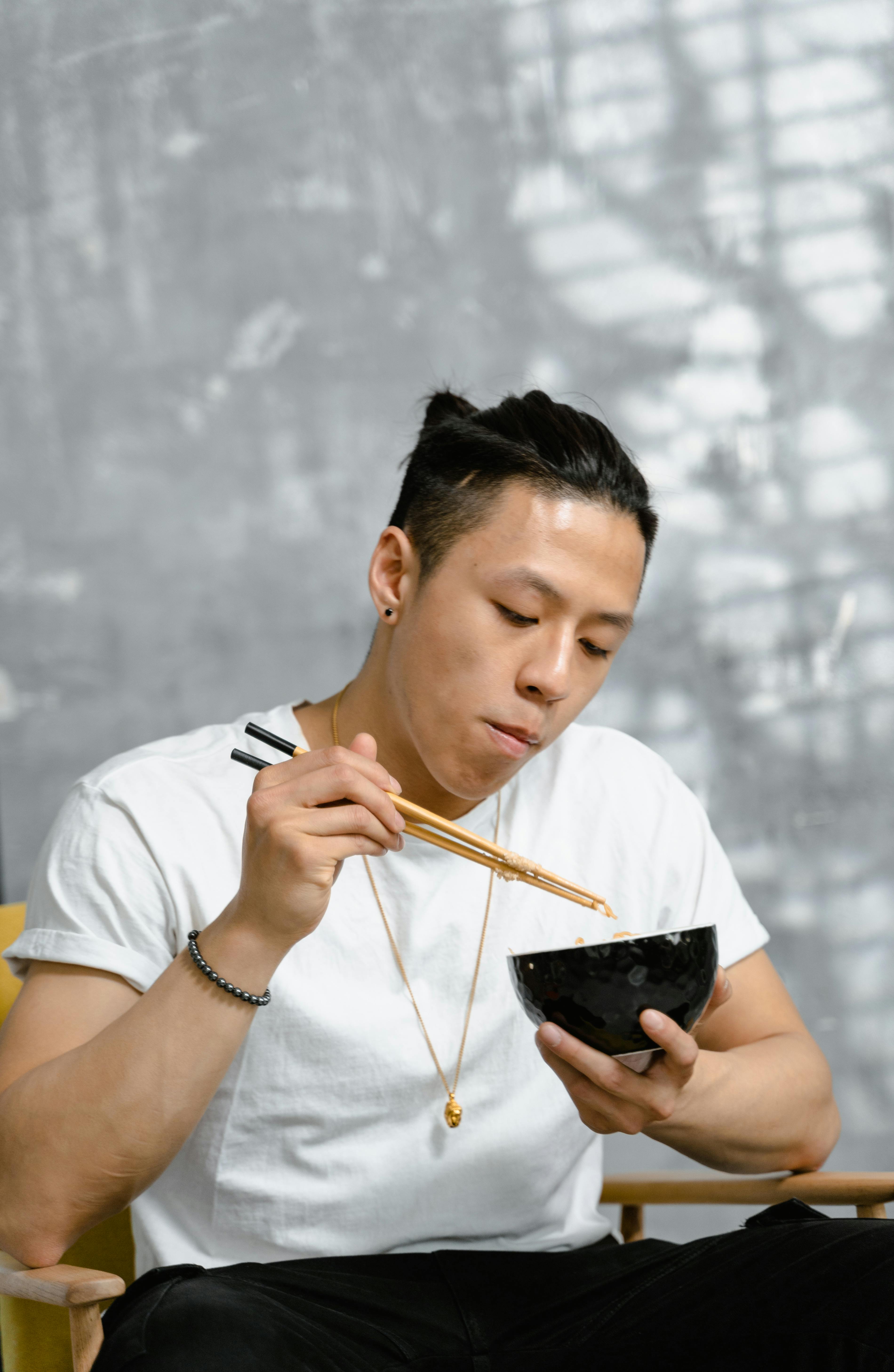 a man in white shirt eating using his chopsticks