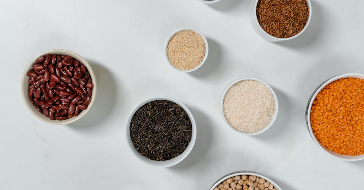 Flat lay of diverse grains and legumes in bowls on a marble surface, highlighting healthy ingredients.