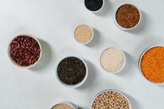 Flat lay of diverse grains and legumes in bowls on a marble surface, highlighting healthy ingredients.