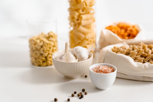 Free Assorted raw pasta with garlic, pink salt, and pepper on a white surface. Stock Photo
