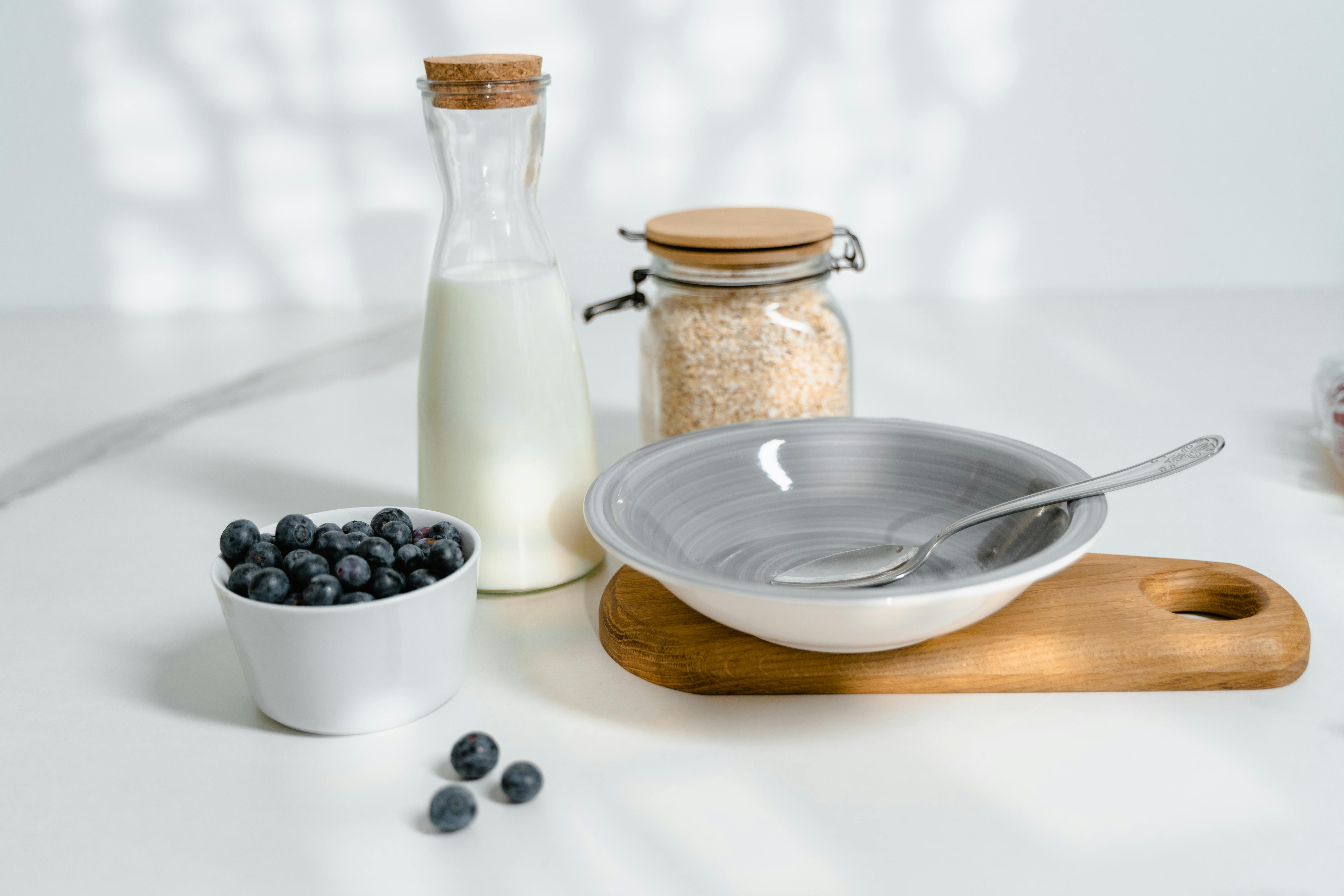 A minimalistic breakfast setup featuring blueberries, milk, and oats on a bright kitchen counter.