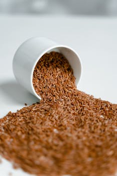 A close-up view of brown rice spilling from a white cup onto a clean surface.