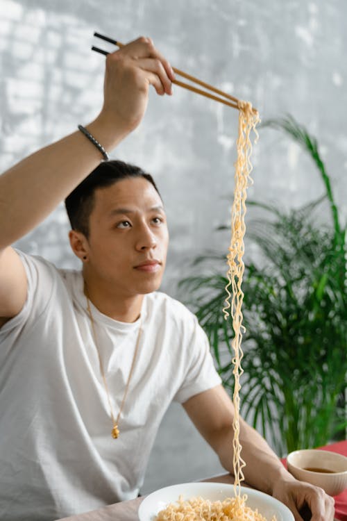 Photo of a Man in a White Collar Neck Shirt Looking at Noodles