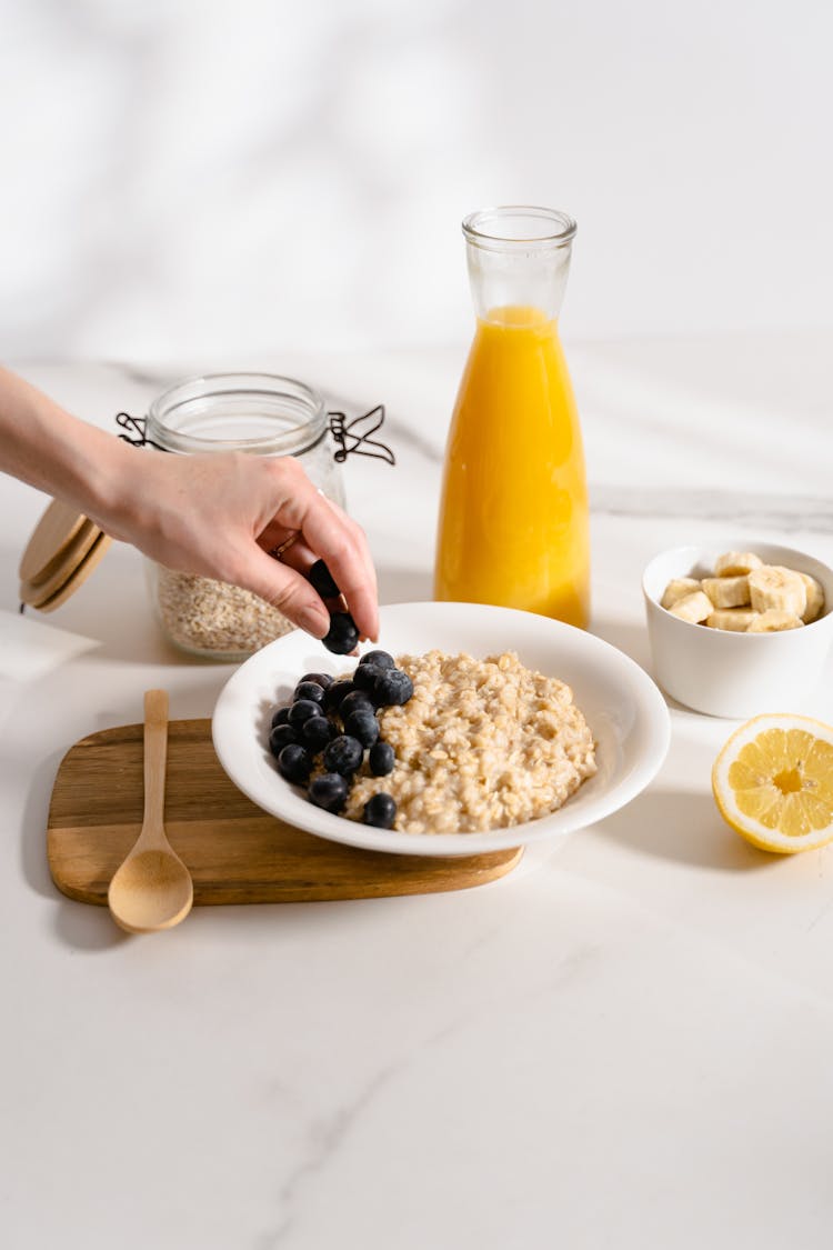 A Person Adding Blueberries On Oats In A Bowl