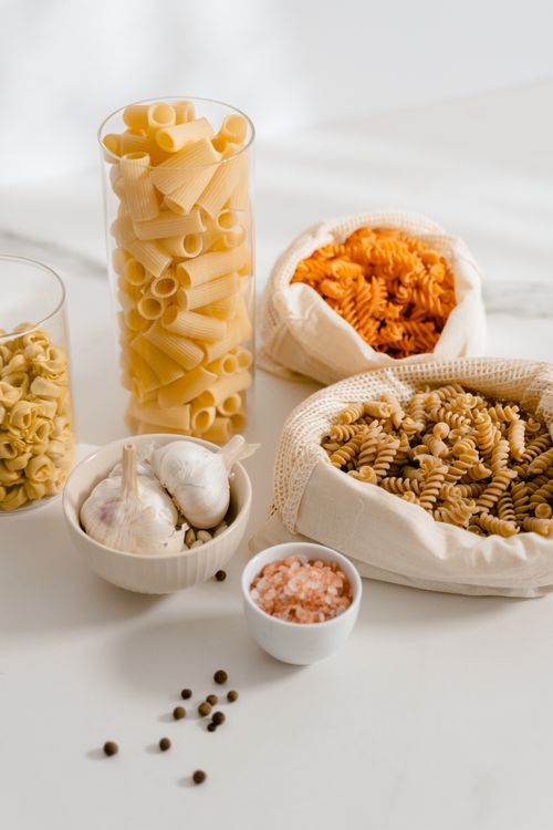 Free Assorted uncooked pasta and ingredients on a marble surface including garlic and pink salt. Stock Photo