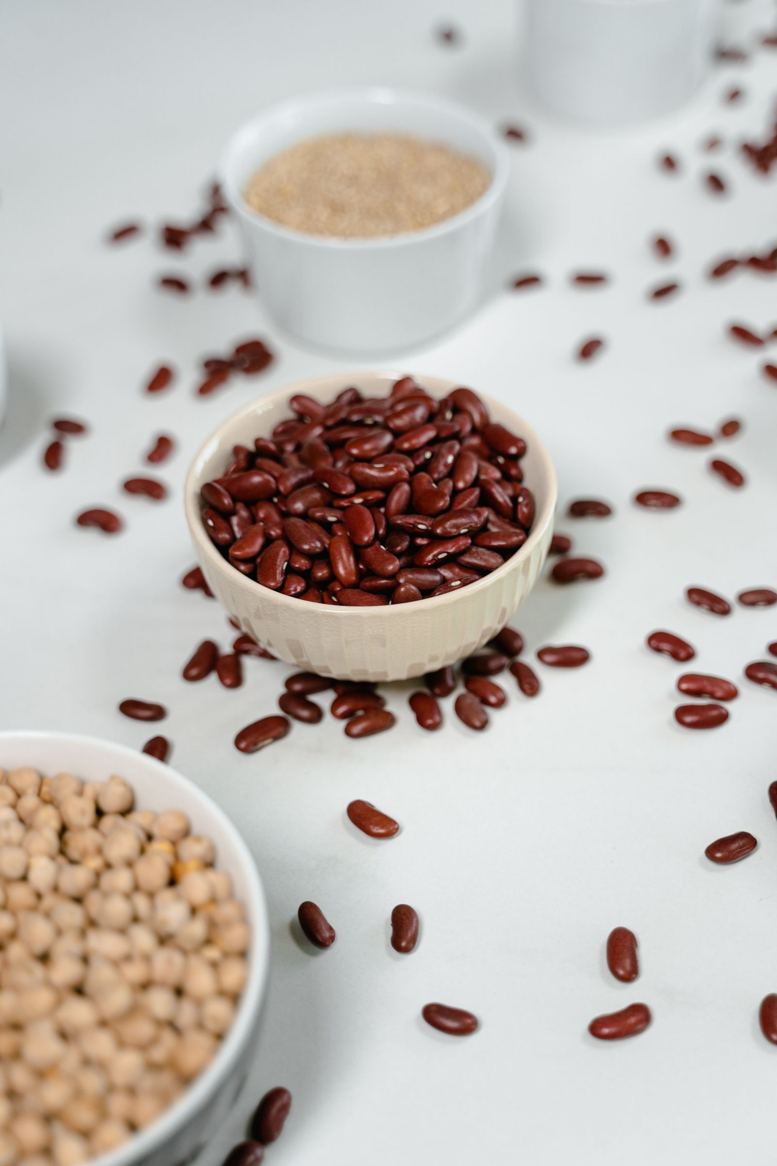 Overhead view of uncooked beans, lentils and grains in small ceramic bowls on a pale surface