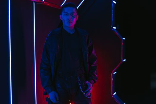 A young man in cyberpunk fashion illuminated by neon lights, showcasing a futuristic style.