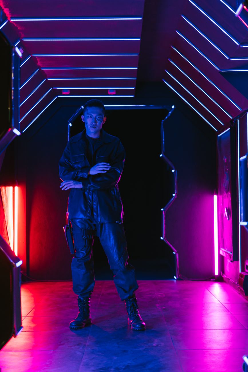 Man in futuristic outfit standing in a neon-lit corridor reflecting a cyberpunk aesthetic.