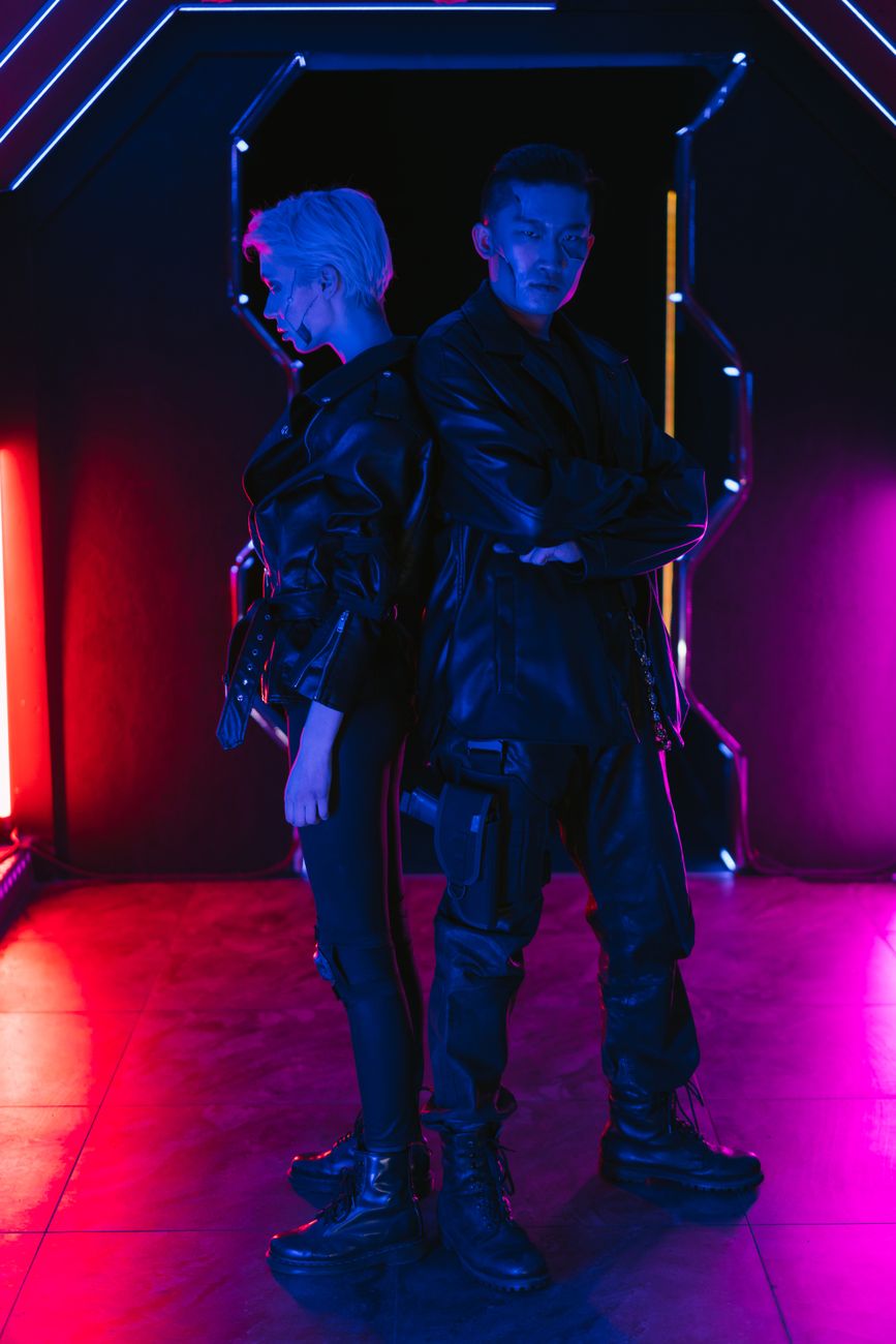 Two people in stylish cyberpunk attire pose in vibrant neon lighting, embodying futuristic fashion.