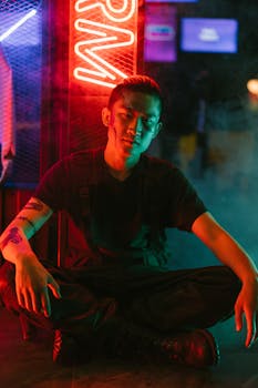 Futuristic cyberpunk portrait featuring an Asian man sitting in neon lighting, showcasing modern fashion.