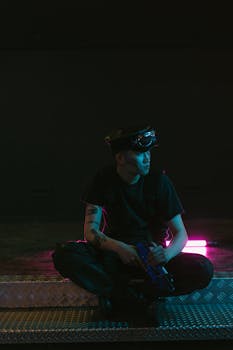 A man with a cyberpunk style sits indoors with neon lighting, exuding a futuristic vibe.