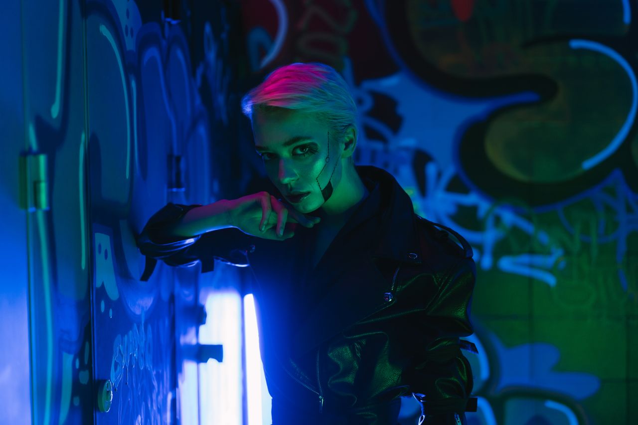person posing in a graffiti filled alley under vibrant neon lights exu