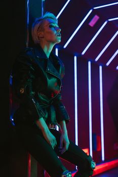 Stylish woman posing in a futuristic nightclub illuminated by vibrant neon lights.