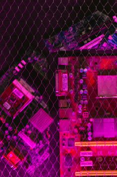 A creatively lit circuit board behind a wire mesh, featuring vibrant pink and red tones.