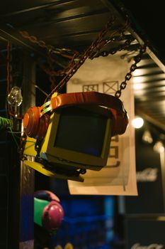 A vintage monitor with oversized headphones suspended in a dimly lit industrial location.