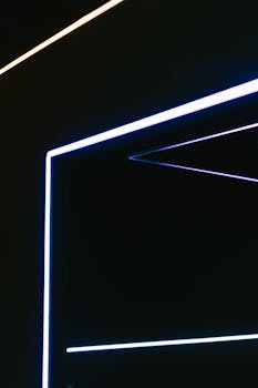 Abstract geometric shapes formed by neon strip lights in dark setting.