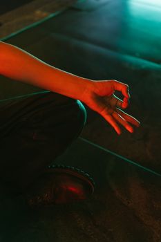 A close-up of a hand in a meditation pose on stairs with colorful gradient lighting, evoking a modern and calm atmosphere.