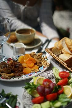 A fresh and colorful brunch setup featuring coffee, fruits, nuts, vegetables, and bread on a sunny day.