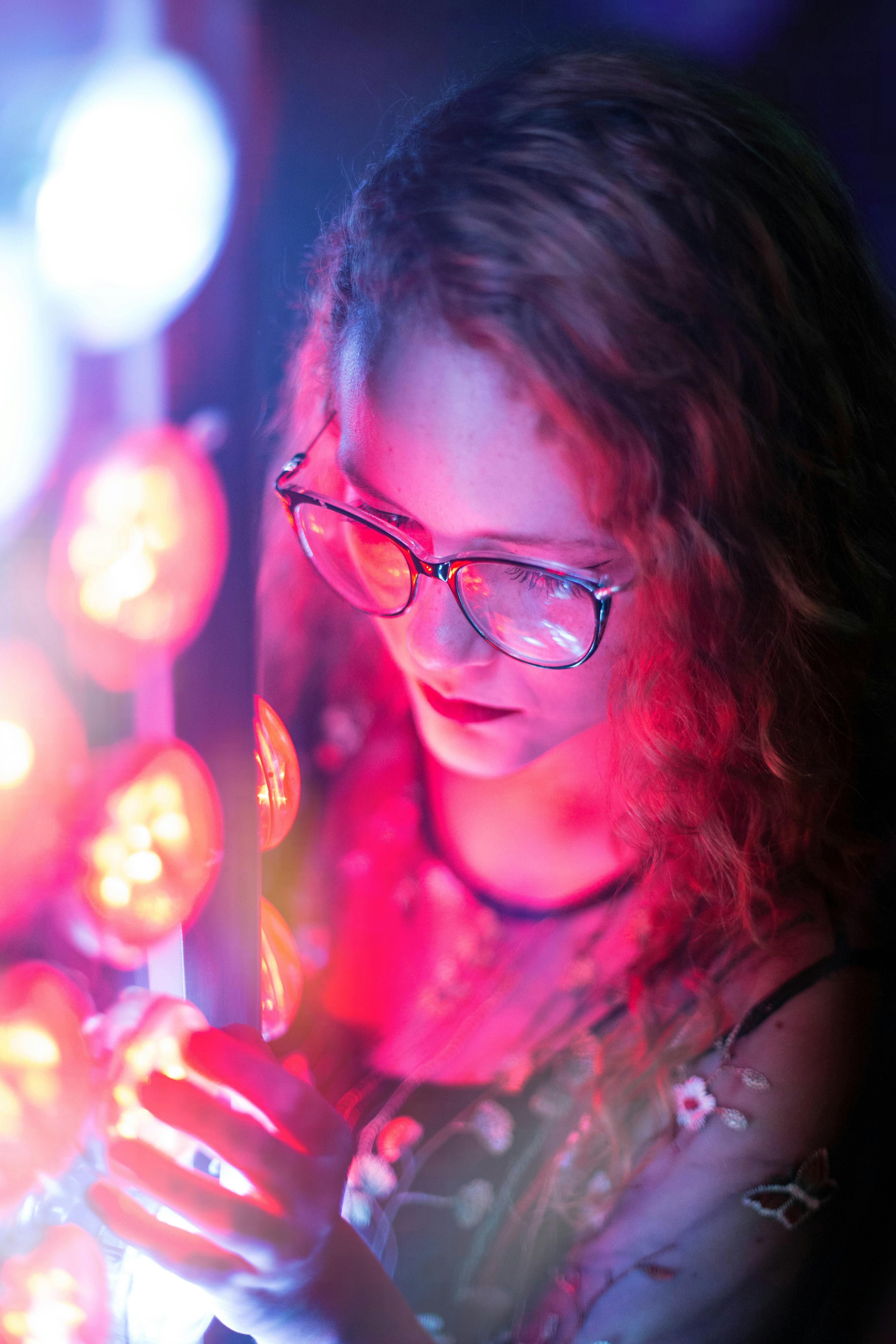 Woman with glasses admiring vibrant neon lights at night.