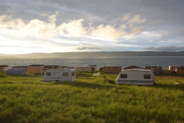 White camper vans parked on green grass overlooking the ocean at a coastal site