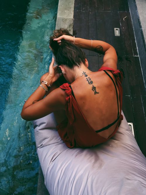 Free Woman in red dress relaxing poolside, showcasing back tattoo. Stock Photo