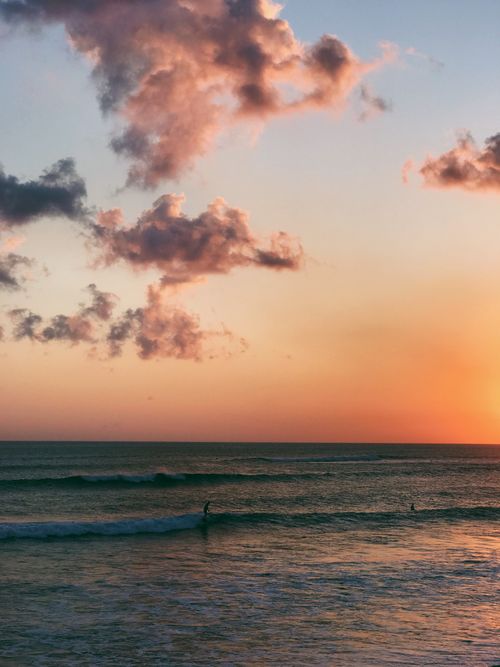 Free A calming sunset over the ocean with a distant surfer gliding along the waves under a colorful sky. Stock Photo